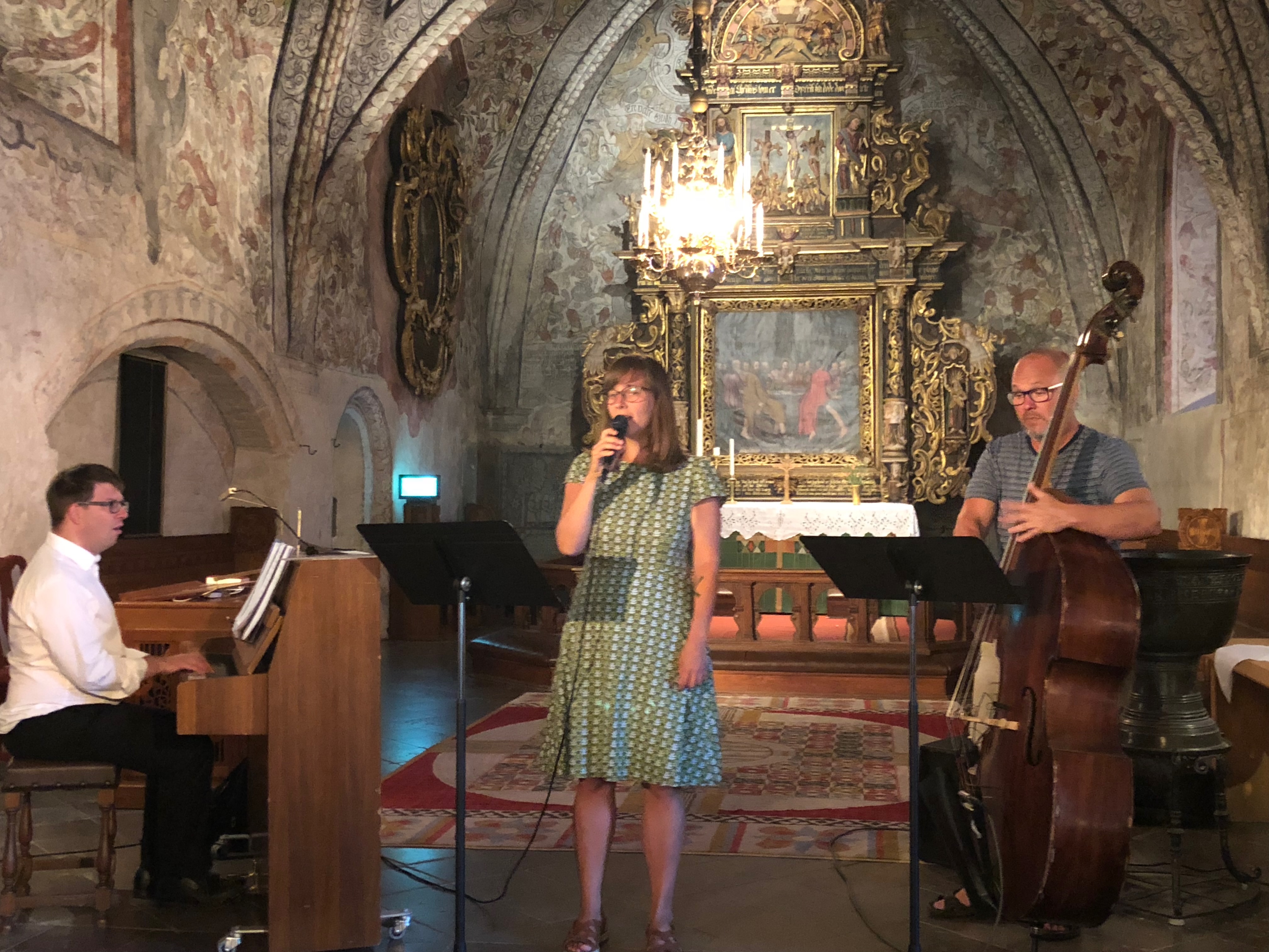 Julia sjunger i en kyrka med målade valv, tillsammans med en pianist och en kontrabasist.